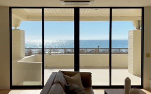 Sliding glass doors open to a beachfront terrace and ocean, shades raised